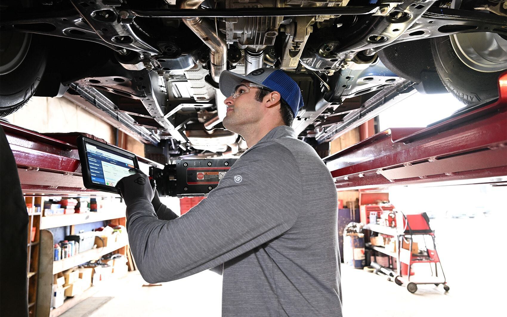 Ase certified technician inspecting vehicle under chassis with tablet
